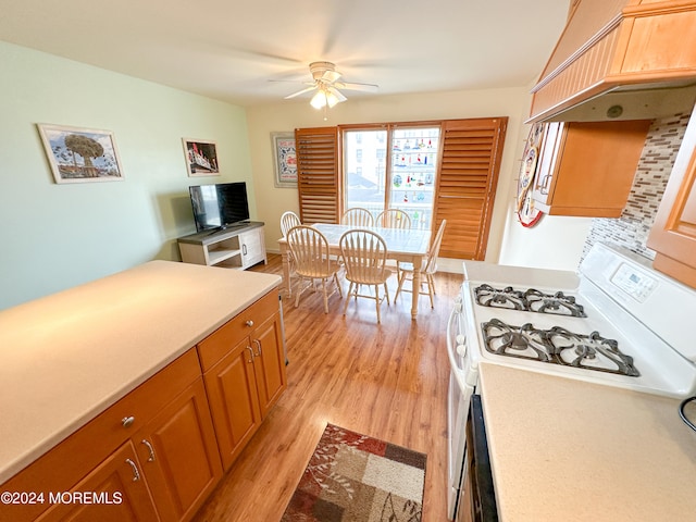 kitchen with light wood-type flooring, ceiling fan, custom range hood, and white range with gas stovetop