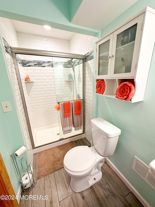 bathroom with wood-type flooring, toilet, and a shower with door