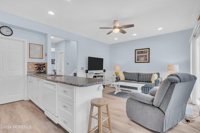 kitchen featuring white dishwasher, sink, white cabinetry, a kitchen breakfast bar, and light hardwood / wood-style floors