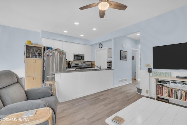 kitchen featuring white cabinets, kitchen peninsula, appliances with stainless steel finishes, dark stone countertops, and light wood-type flooring