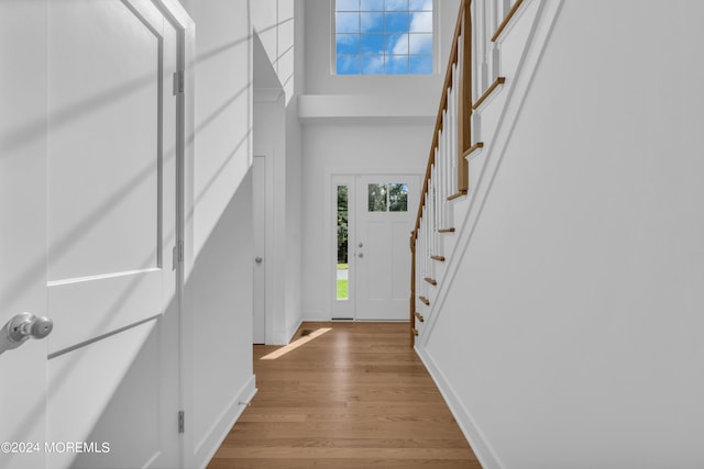 foyer entrance featuring stairs, light wood-style flooring, a towering ceiling, and baseboards