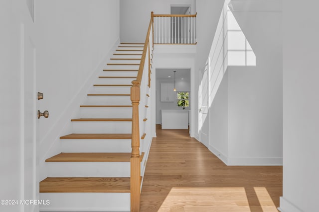 staircase featuring a towering ceiling, baseboards, and wood finished floors