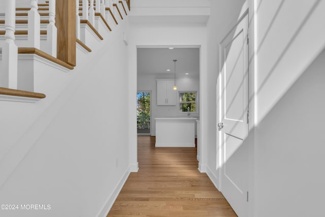 corridor with light wood-type flooring, stairway, baseboards, and recessed lighting