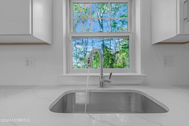 details with light stone countertops, white cabinetry, and a sink