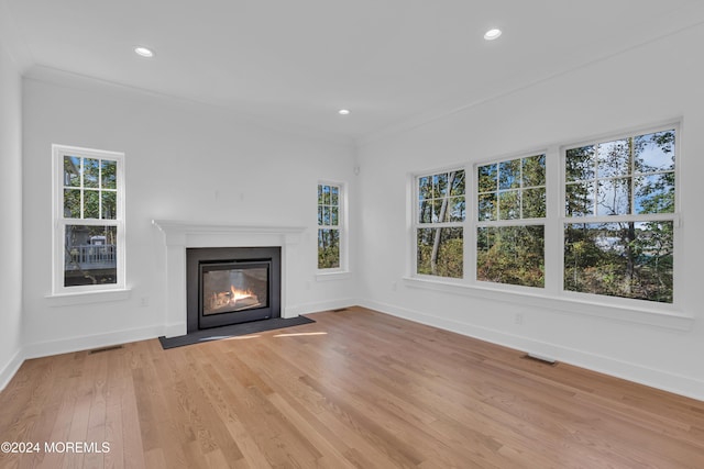 unfurnished living room featuring a fireplace with flush hearth, visible vents, ornamental molding, and light wood finished floors