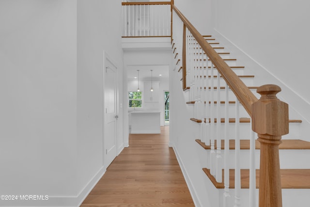 stairs featuring wood finished floors, a towering ceiling, and baseboards