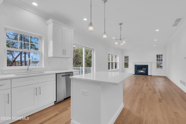 kitchen featuring hanging light fixtures, light countertops, stainless steel dishwasher, white cabinetry, and a sink