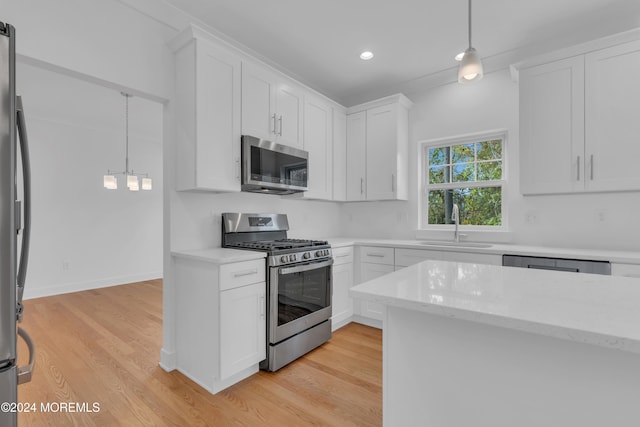 kitchen featuring light wood-style flooring, appliances with stainless steel finishes, decorative light fixtures, white cabinetry, and a sink