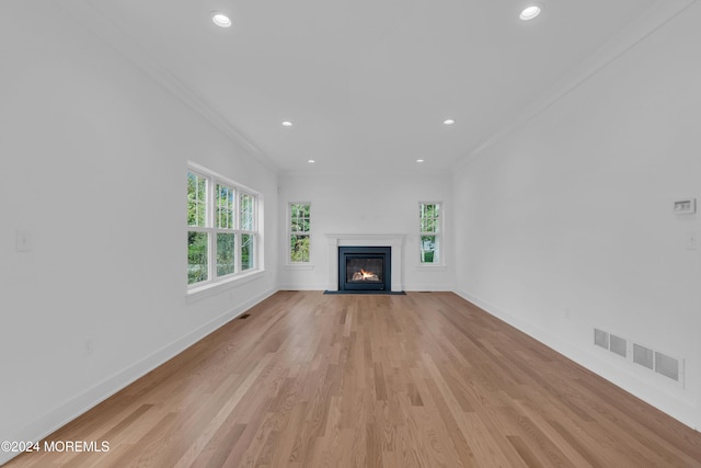 unfurnished living room with light wood-style floors, visible vents, crown molding, and baseboards