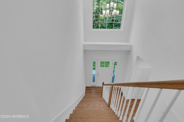 stairway featuring baseboards, wood finished floors, a wealth of natural light, and a notable chandelier