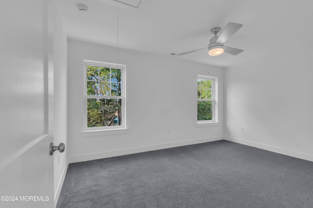 empty room featuring attic access, dark colored carpet, and baseboards