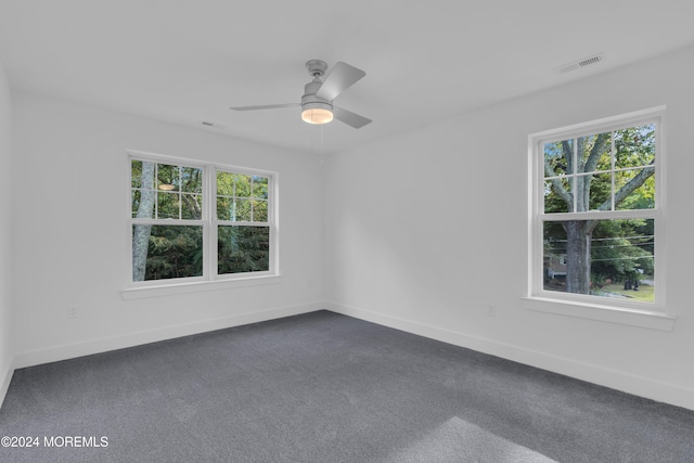 unfurnished room featuring a ceiling fan, dark colored carpet, visible vents, and baseboards