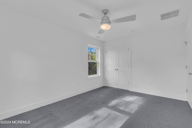 empty room featuring ceiling fan, dark carpet, visible vents, and baseboards