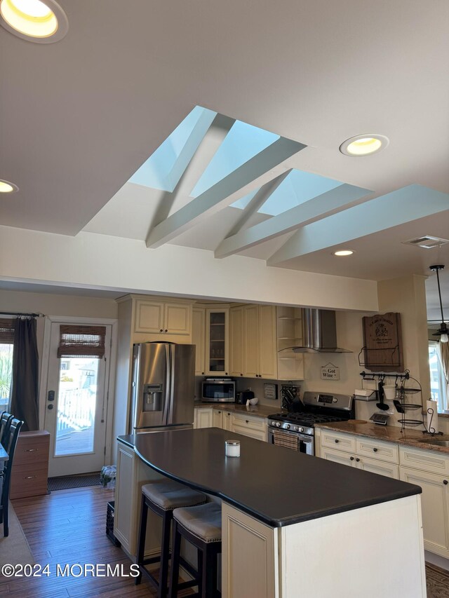 kitchen featuring a kitchen island, stainless steel appliances, wall chimney exhaust hood, dark wood-type flooring, and vaulted ceiling with skylight