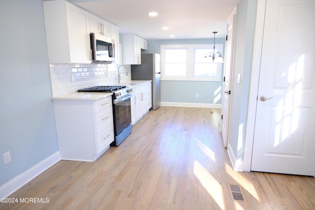 kitchen featuring backsplash, white cabinets, appliances with stainless steel finishes, a notable chandelier, and light hardwood / wood-style floors