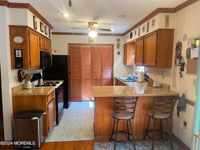 kitchen featuring light wood-type flooring, kitchen peninsula, ornamental molding, black appliances, and a kitchen bar