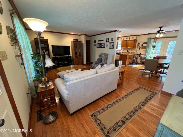 living room featuring ceiling fan, ornamental molding, a textured ceiling, and hardwood / wood-style floors