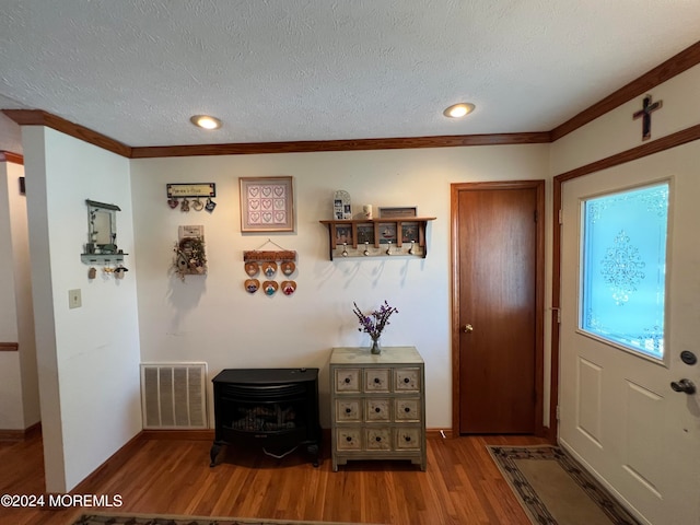 entrance foyer with crown molding, hardwood / wood-style floors, a textured ceiling, and a wood stove