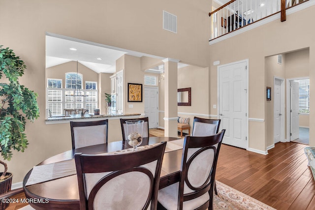 dining space featuring high vaulted ceiling, decorative columns, wood-type flooring, and a chandelier