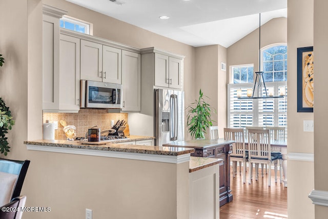 kitchen featuring kitchen peninsula, stainless steel appliances, vaulted ceiling, light stone counters, and light hardwood / wood-style floors