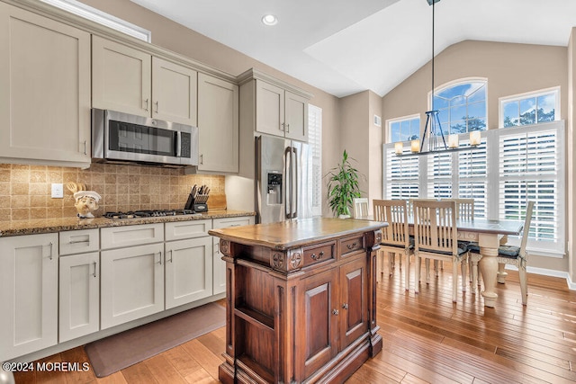 kitchen with vaulted ceiling, hanging light fixtures, stainless steel appliances, and light hardwood / wood-style floors