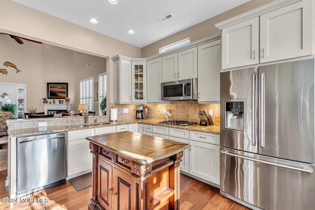 kitchen with sink, white cabinets, light wood-type flooring, appliances with stainless steel finishes, and light stone counters