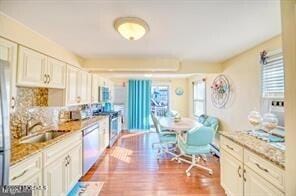 kitchen featuring sink, tasteful backsplash, wood-type flooring, white cabinetry, and stainless steel appliances