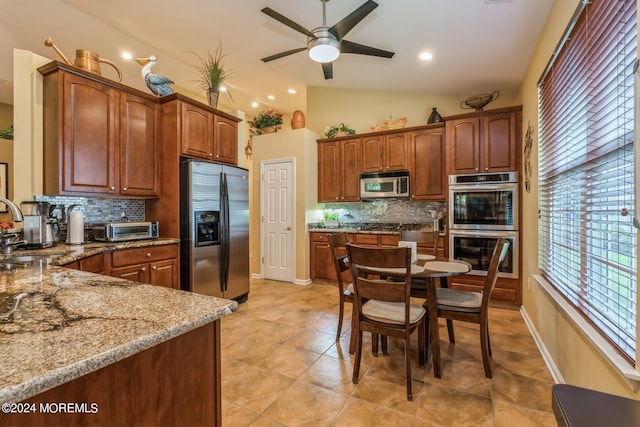 kitchen featuring appliances with stainless steel finishes, light stone counters, decorative backsplash, and vaulted ceiling