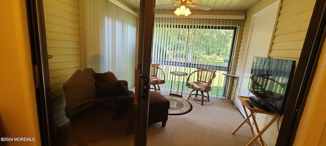 living area featuring ceiling fan, wood walls, and carpet