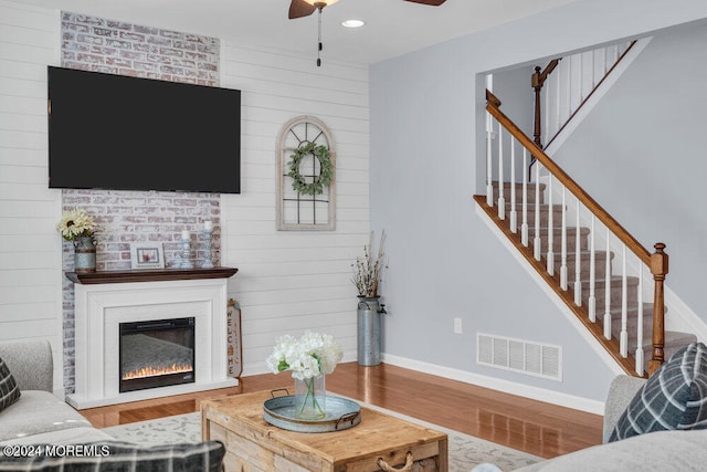 living room featuring ceiling fan, hardwood / wood-style floors, and a large fireplace