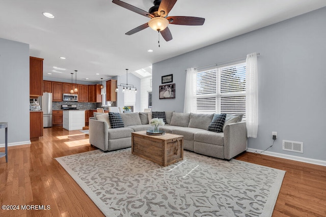 living room with ceiling fan with notable chandelier and light hardwood / wood-style floors