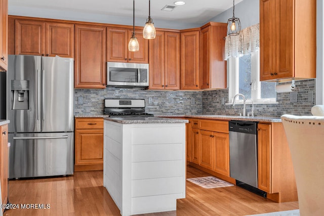 kitchen with appliances with stainless steel finishes, decorative light fixtures, and light hardwood / wood-style floors