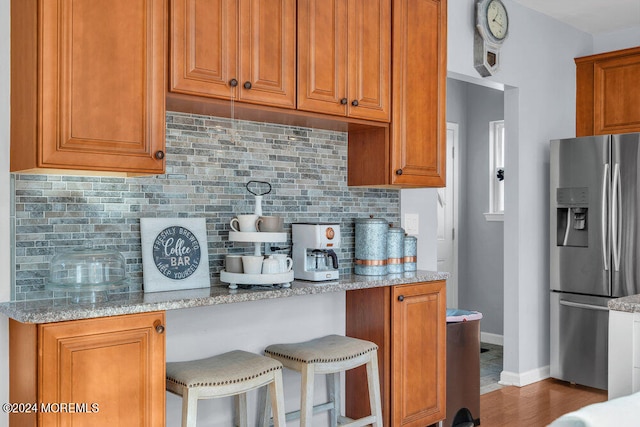 kitchen featuring light stone counters, wood-type flooring, a breakfast bar area, and stainless steel fridge with ice dispenser