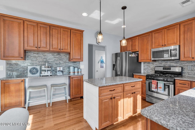 kitchen featuring appliances with stainless steel finishes, hanging light fixtures, a center island, and light hardwood / wood-style floors