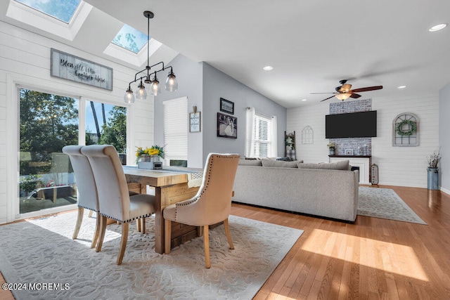 dining room featuring ceiling fan, light wood-type flooring, lofted ceiling, and a large fireplace