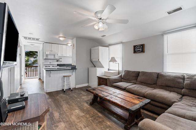 living room with stacked washer / drying machine, dark wood-type flooring, and ceiling fan