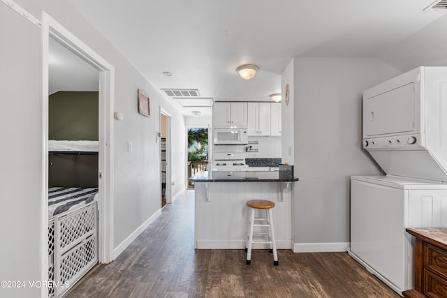 kitchen with dark hardwood / wood-style flooring, a kitchen breakfast bar, white cabinetry, stacked washer and clothes dryer, and white appliances