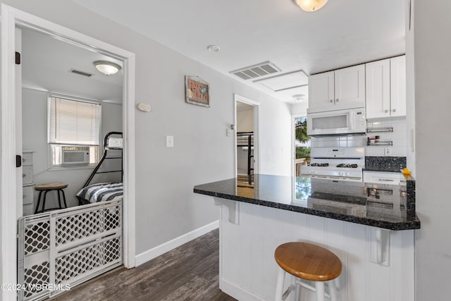 kitchen with a breakfast bar area, dark wood-type flooring, dark stone countertops, white cabinetry, and white appliances