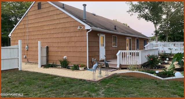 property exterior at dusk with a deck and a lawn