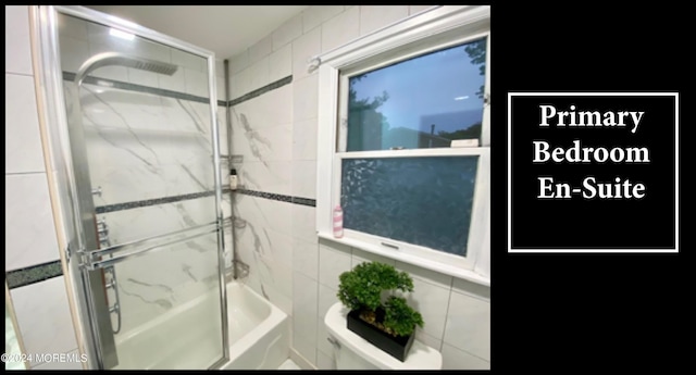 bathroom with toilet and shower / bath combination with glass door