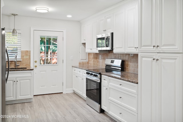 kitchen with tasteful backsplash, stainless steel appliances, white cabinets, dark stone countertops, and light hardwood / wood-style flooring