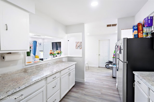 kitchen featuring light hardwood / wood-style flooring, light stone counters, stainless steel fridge, and white cabinets