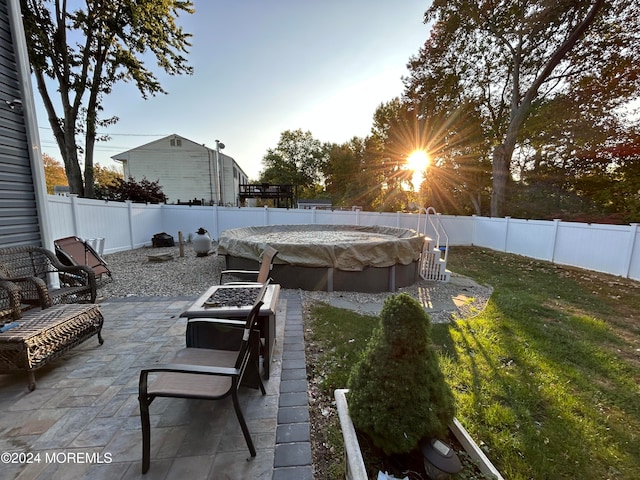 patio terrace at dusk featuring an outdoor fire pit and a lawn