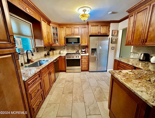 kitchen featuring tasteful backsplash, light stone counters, appliances with stainless steel finishes, ornamental molding, and sink