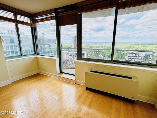 unfurnished room with radiator, wood finished floors, baseboards, and a city view