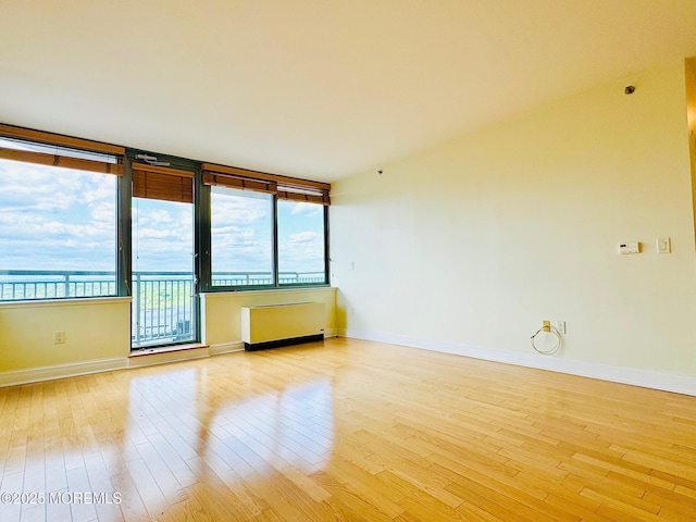 unfurnished room with light wood finished floors, baseboards, and radiator heating unit