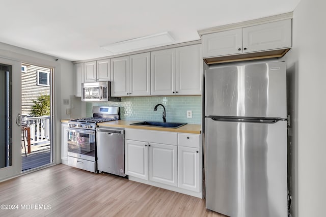 kitchen with stainless steel appliances, white cabinets, sink, light hardwood / wood-style floors, and backsplash