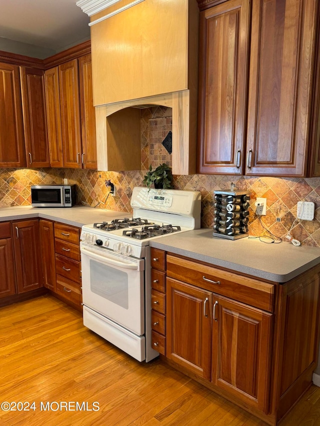 kitchen with light wood-type flooring, white gas range, and tasteful backsplash