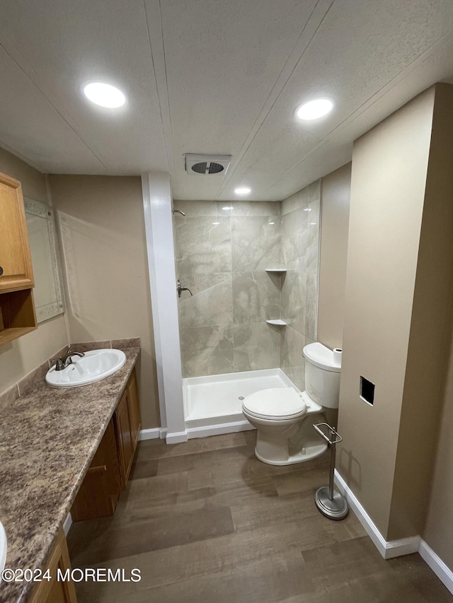 bathroom featuring a tile shower, wood-type flooring, a textured ceiling, toilet, and vanity