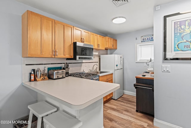 kitchen with kitchen peninsula, backsplash, sink, light hardwood / wood-style floors, and stainless steel appliances